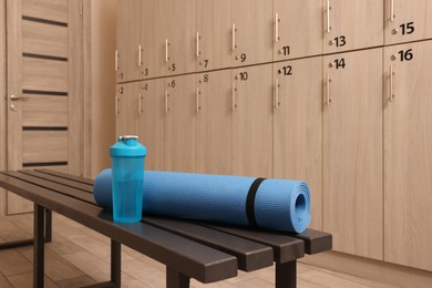Photo of Shaker with water and yoga mat on wooden bench in locker room