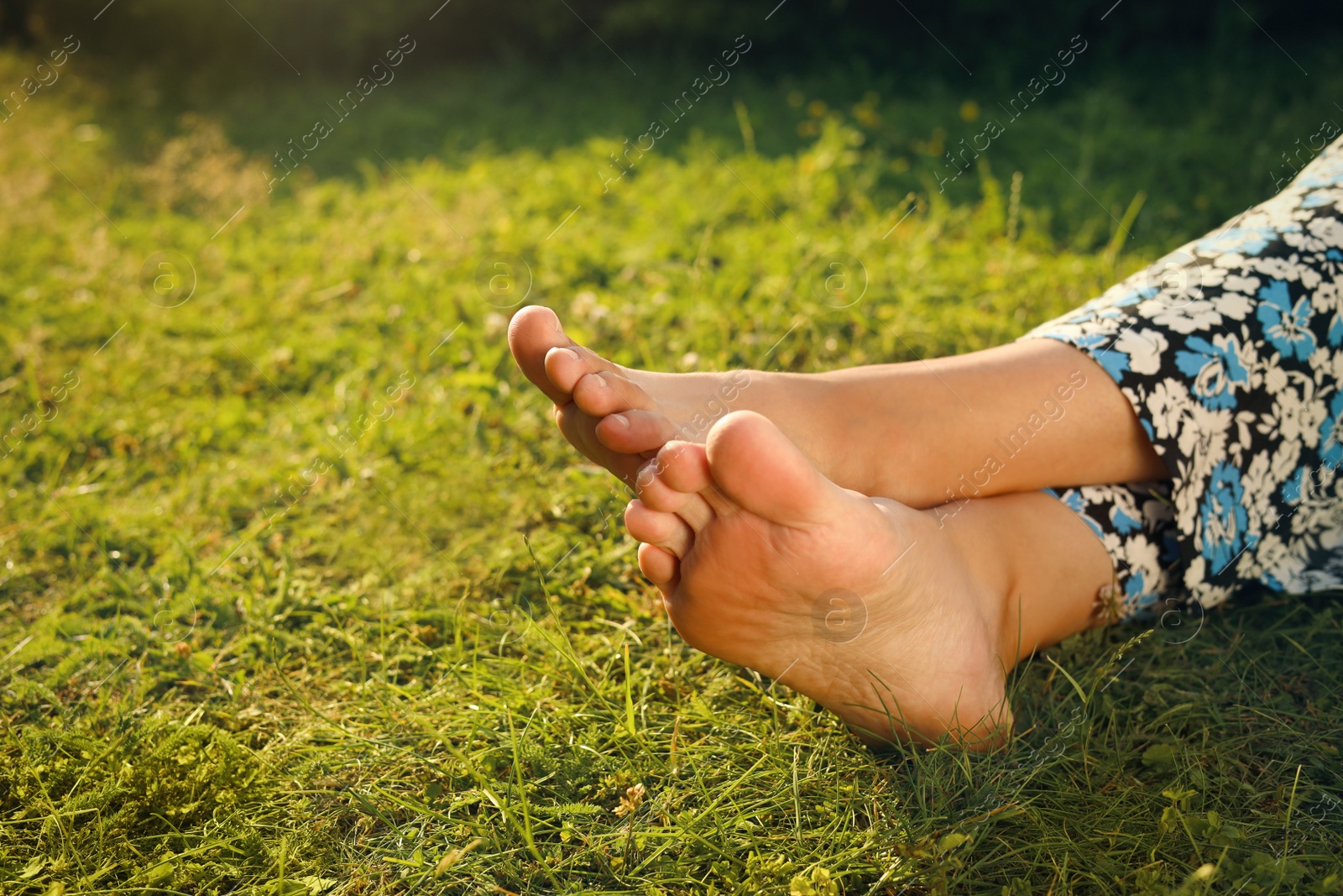 Photo of Woman relaxing barefoot on green grass, closeup. Space for text