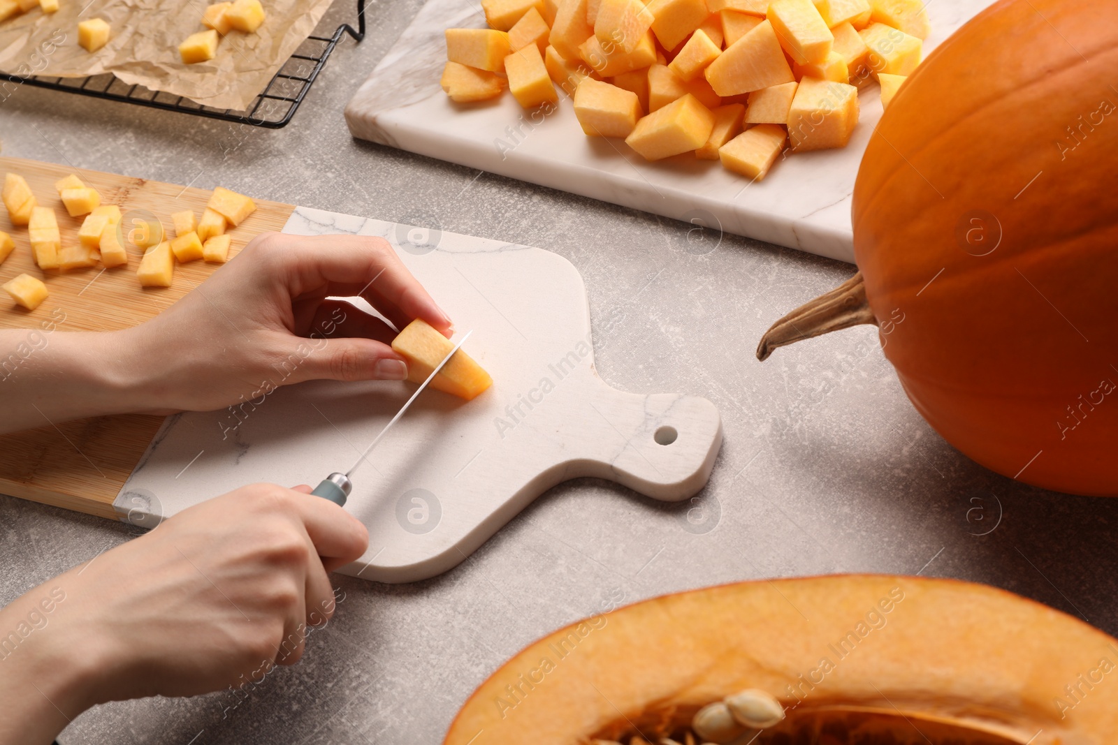 Photo of Woman cutting fresh pumpkin at light grey table, closeup