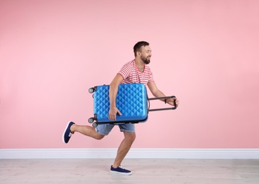 Photo of Man with suitcase running near color wall. Vacation travel