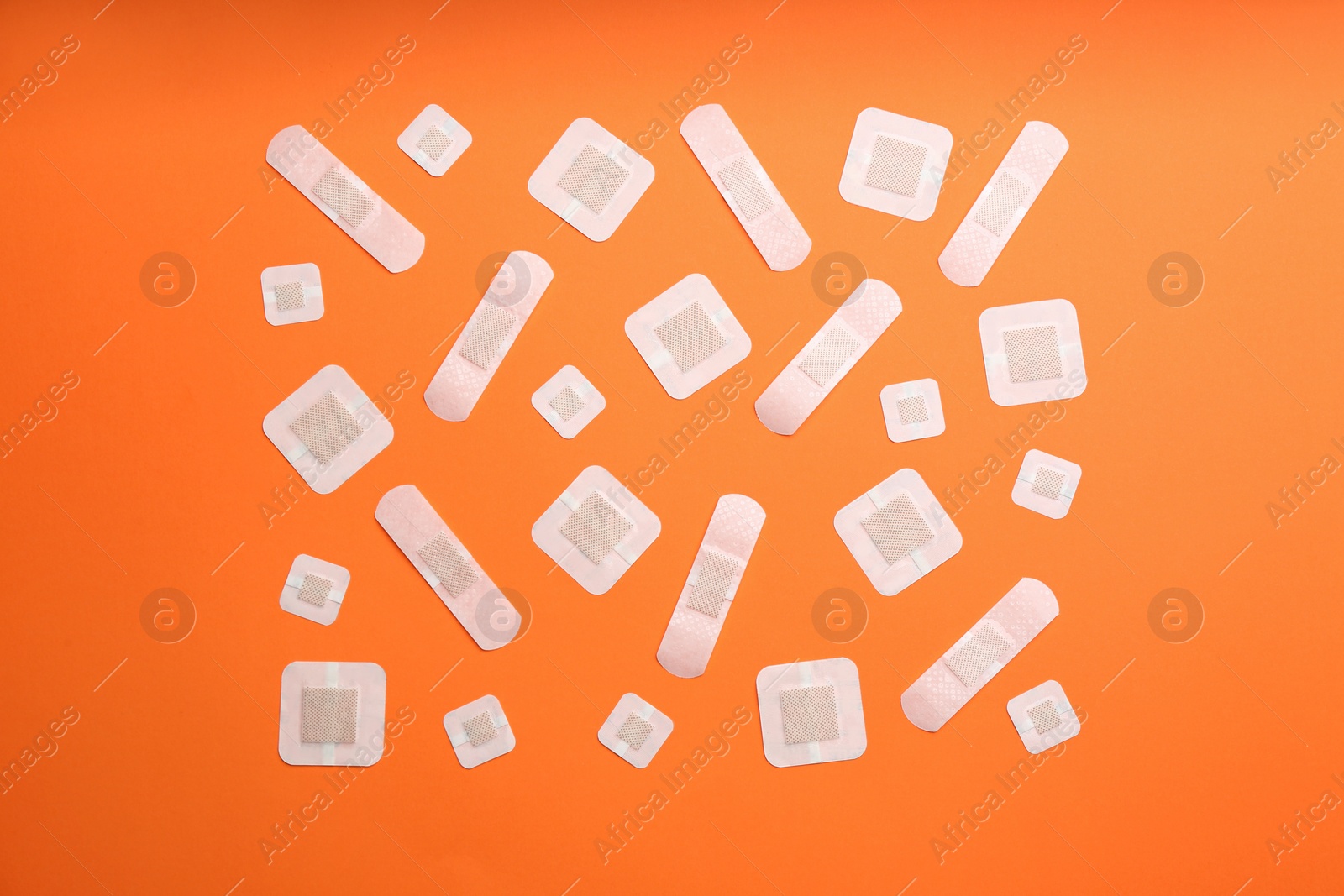 Photo of Different types of sticking plasters on orange background, flat lay