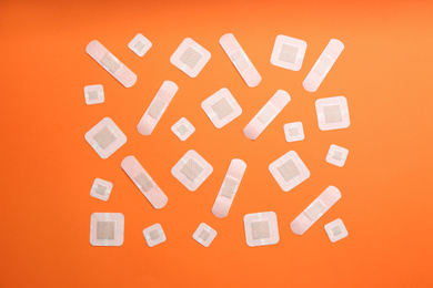Photo of Different types of sticking plasters on orange background, flat lay