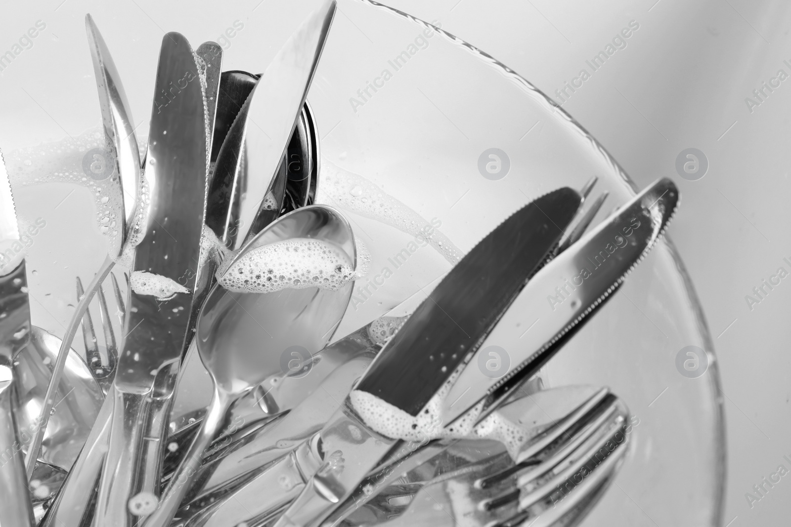 Photo of Washing silver spoons, forks and knives in kitchen sink with water, closeup