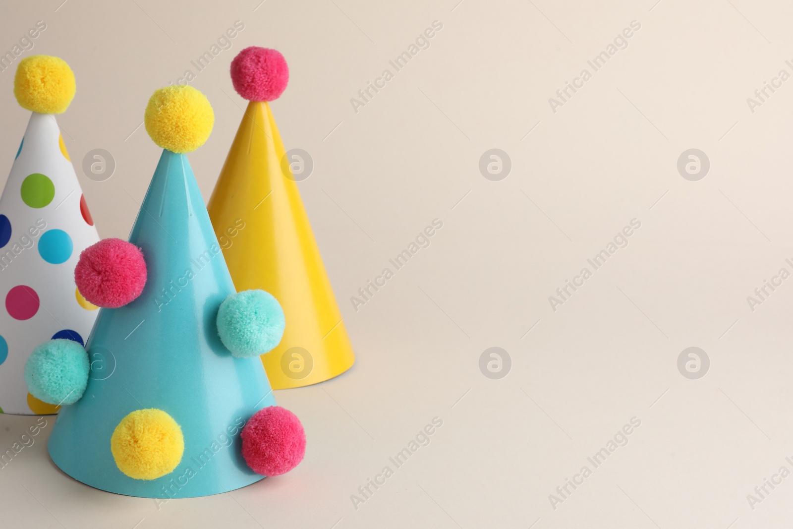 Photo of Colorful party hats with pompoms on beige background. Space for text