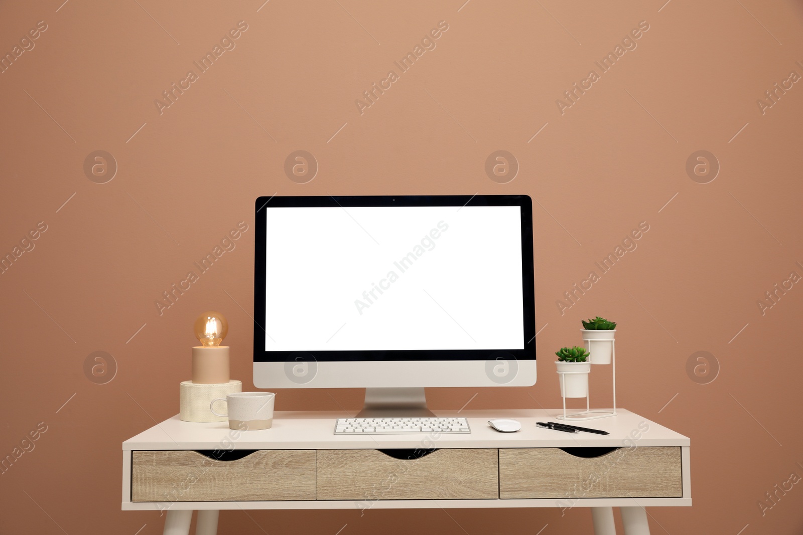 Photo of Comfortable workplace with blank computer display on desk near light brown wall. Space for text