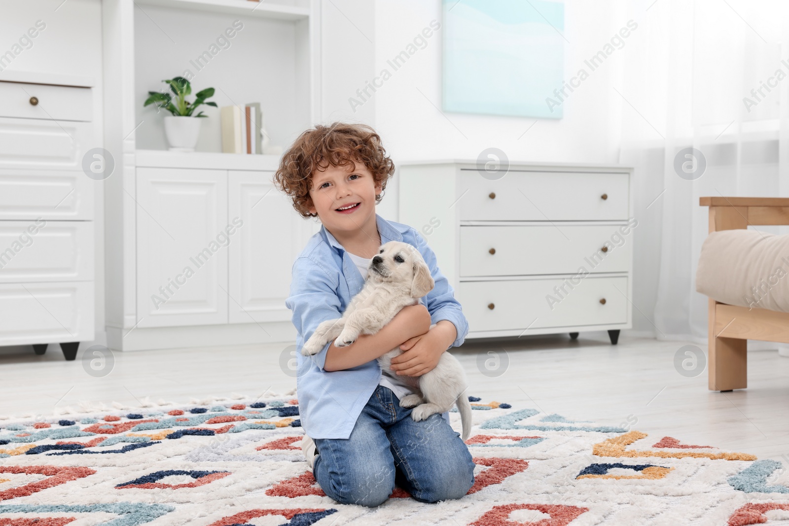 Photo of Little boy with cute puppy on carpet at home