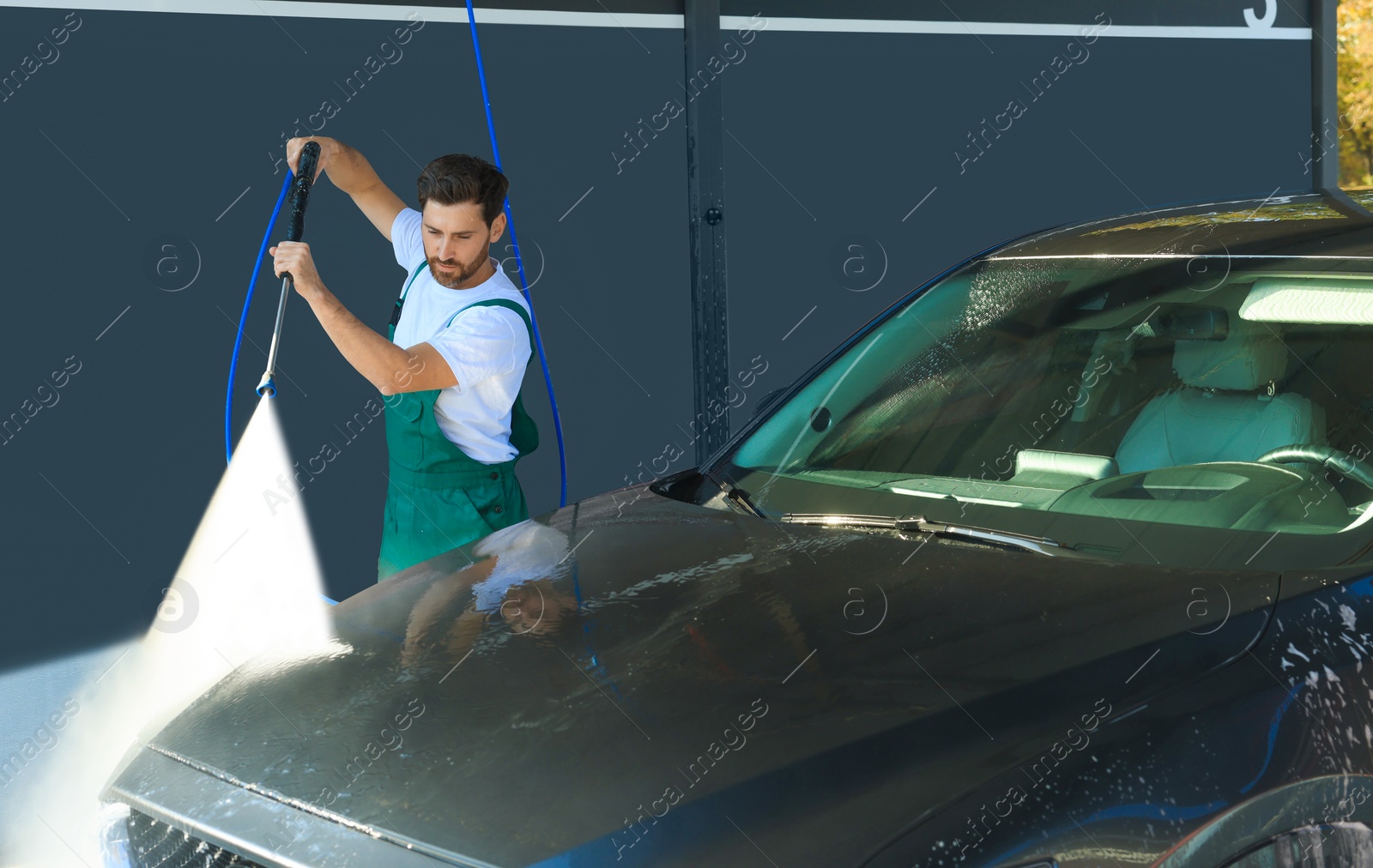 Photo of Worker washing auto with high pressure water jet at outdoor car wash