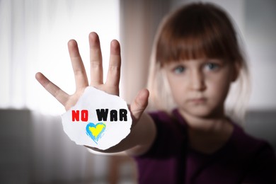 Image of Unhappy little girl showing palm with phrase No War at home, focus on hand