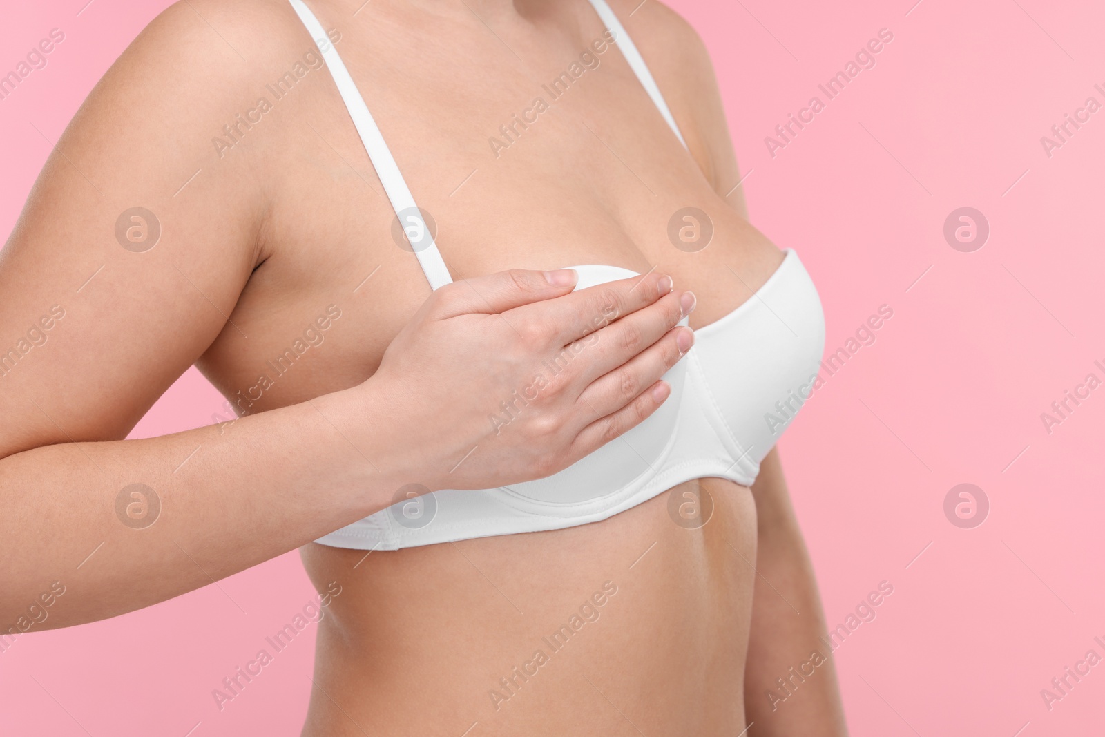 Photo of Mammology. Woman in bra doing breast self-examination on pink background, closeup