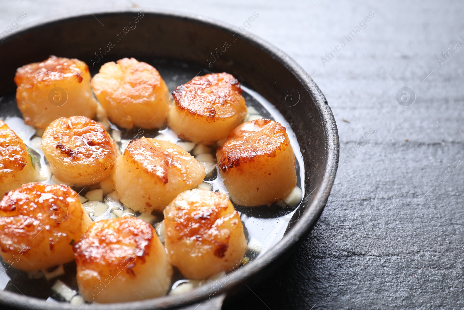 Photo of Delicious fried scallops in dish on dark gray textured table, closeup
