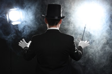 Photo of Magician with wand in smoke on stage, back view