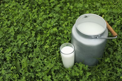 Photo of Can and glass with fresh milk on green grass outdoors, space for text