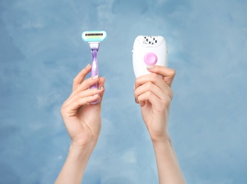 Woman holding modern epilator and razor on color background, closeup