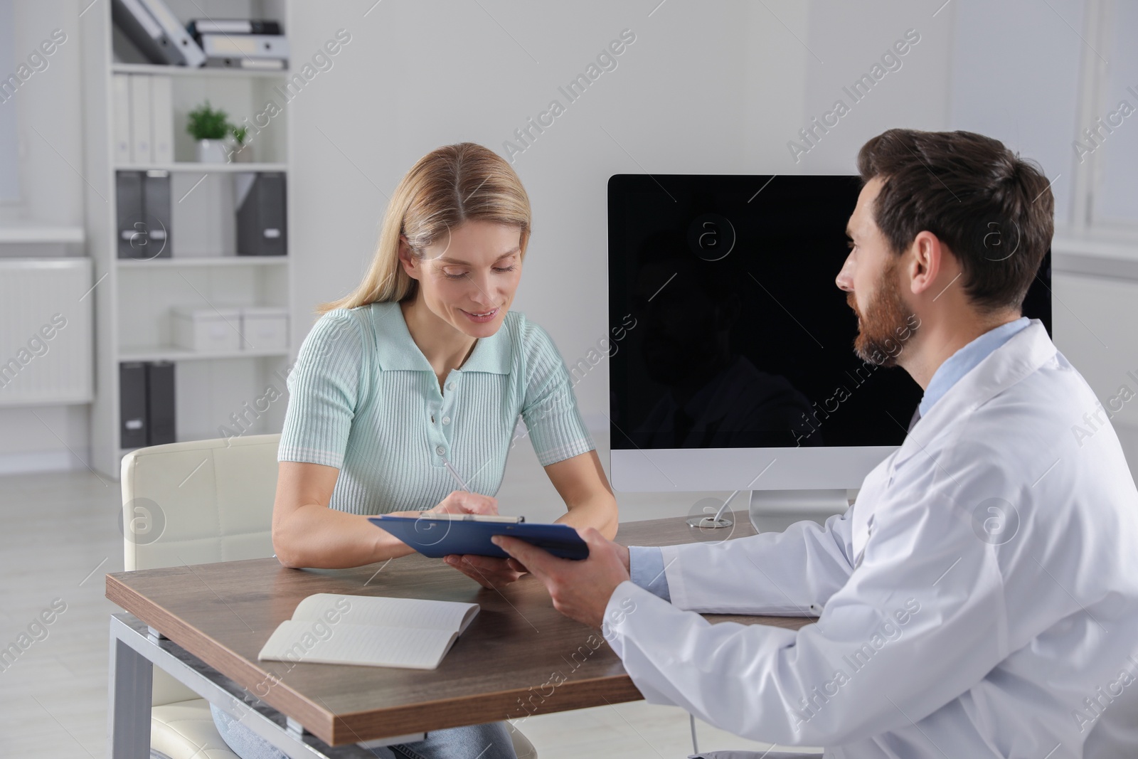 Photo of Doctor consulting patient at wooden table in clinic