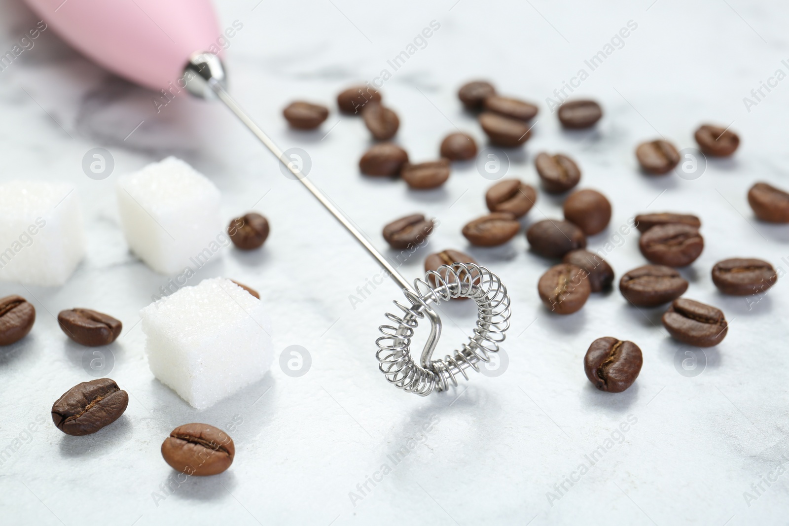 Photo of Pink milk frother wand, sugar cubes and coffee beans on white marble table, closeup