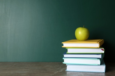 Photo of Books and apple on grey table near chalkboard, space for text. School education