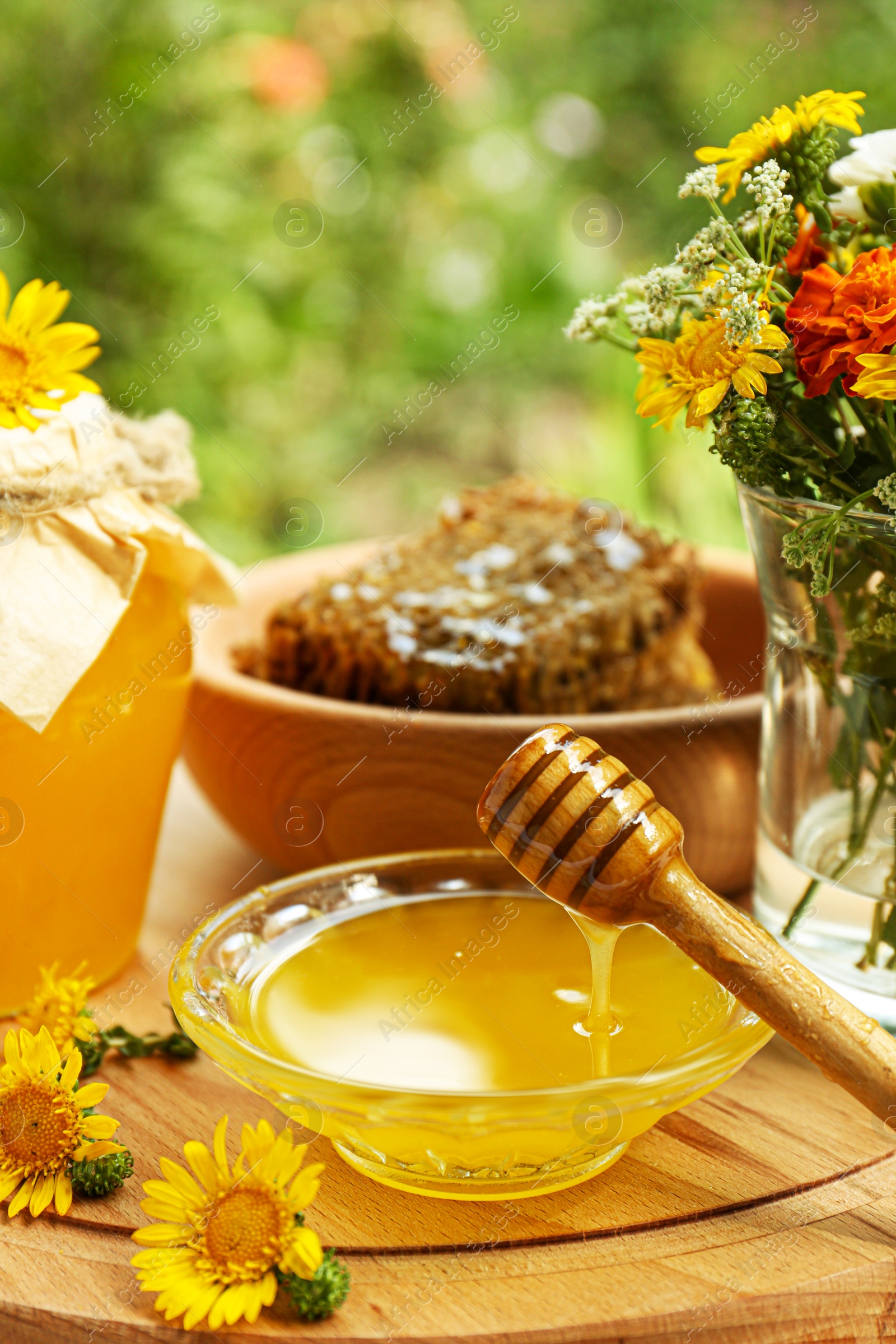 Photo of Delicious honey flowing down from dipper into bowl on wooden board in garden