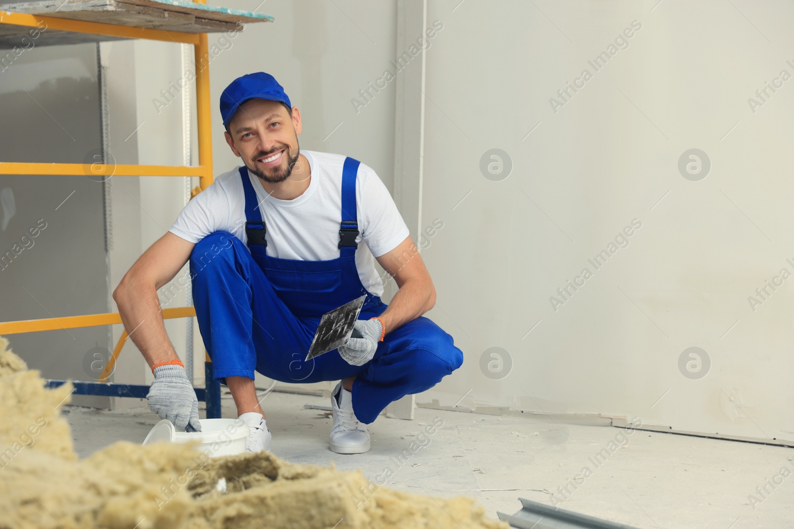 Photo of Professional worker with plaster and putty knife indoors
