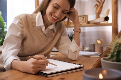 Photo of Young woman drawing in sketchbook with pencil at wooden table indoors, focus on hand
