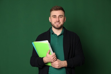 Portrait of young teacher with notebooks on green background