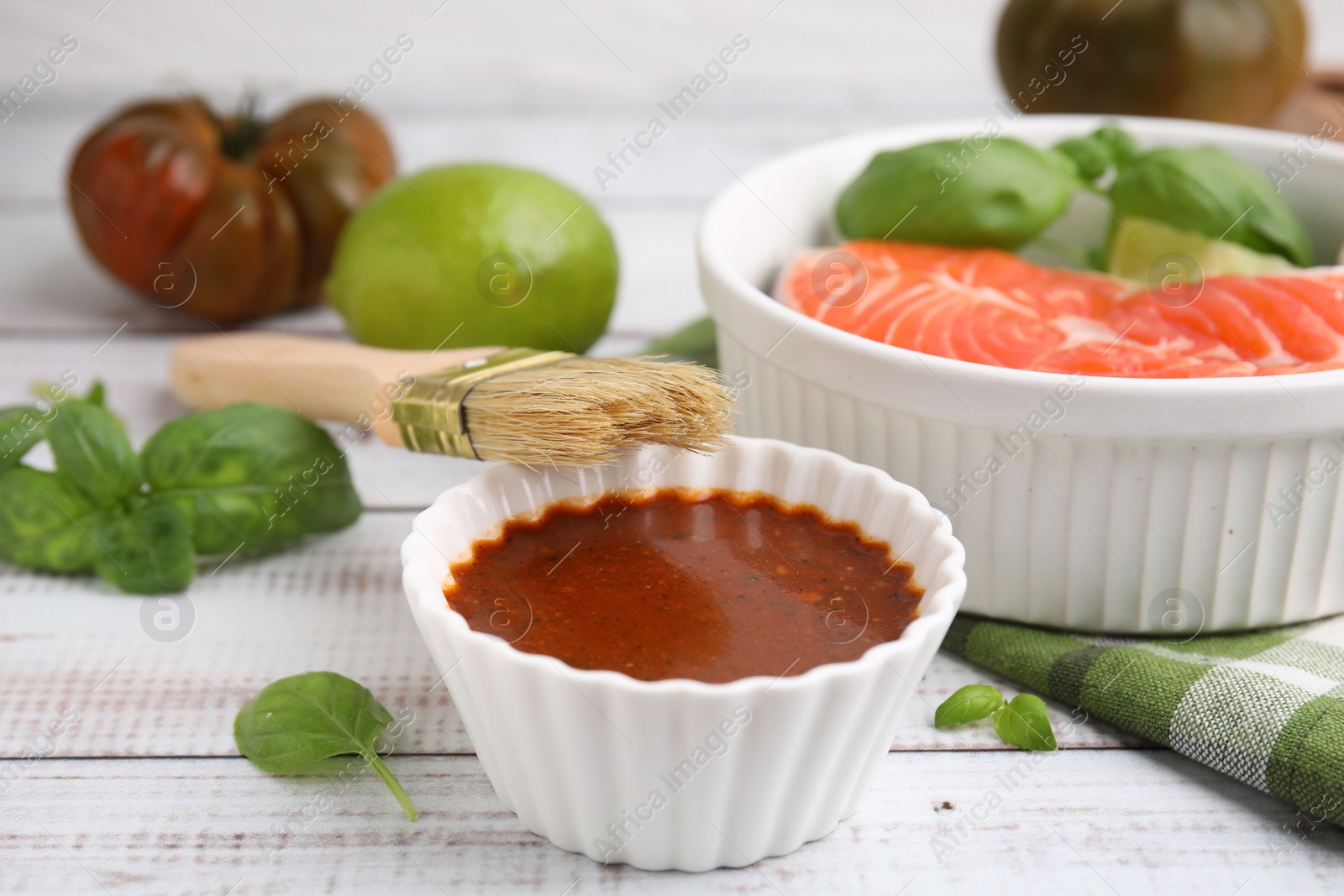 Photo of Fresh marinade, fish, brush and basil on white wooden table, closeup