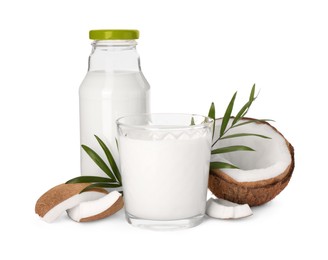 Photo of Glass and bottle of delicious vegan milk, coconut pieces with green leaves on white background