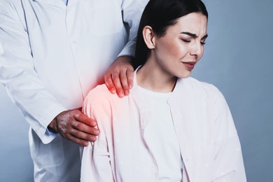 Image of Doctor examining woman with shoulder pain on grey background