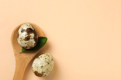 Wooden spoon, speckled quail eggs and green leaf on beige background, flat lay. Space for text