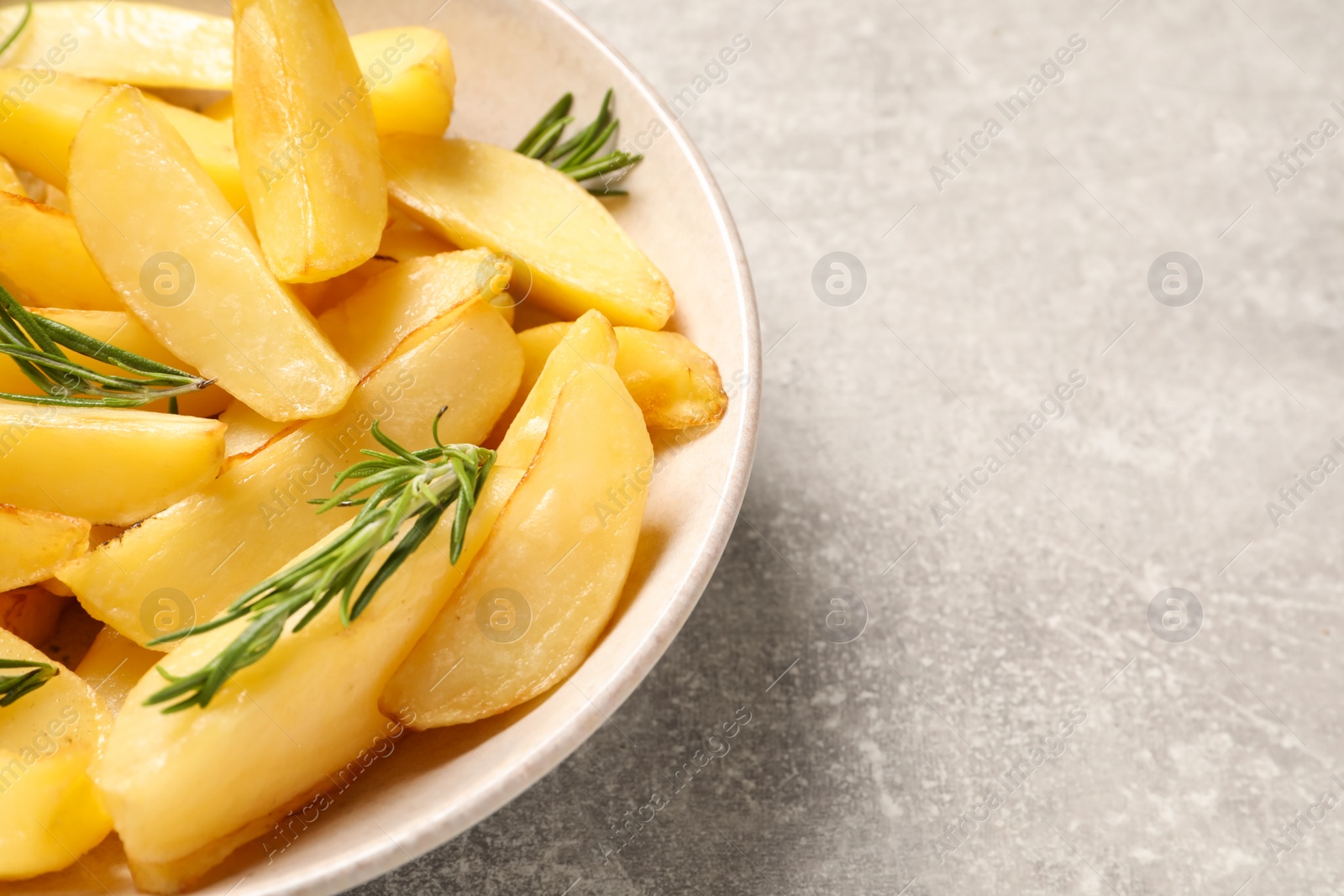 Photo of Plate with tasty baked potato wedges and rosemary on grey table, closeup. Space for text