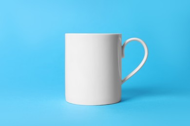 Photo of One white ceramic mug on light blue background