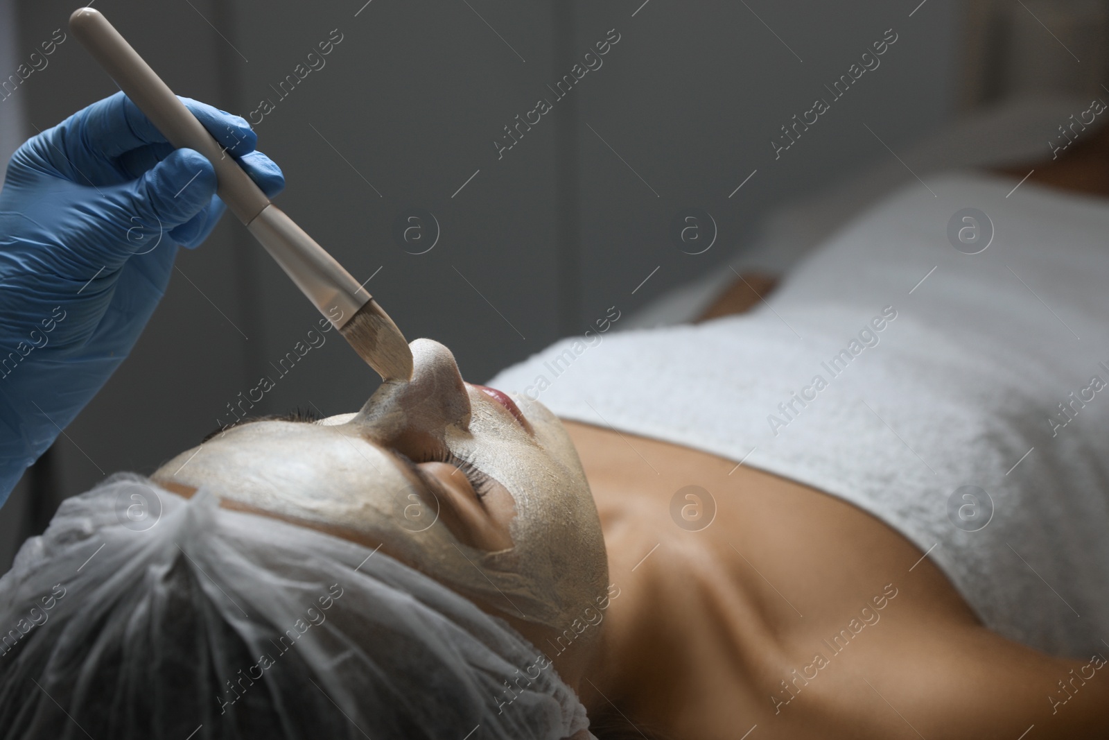 Photo of Cosmetologist applying mask on client's face in spa salon