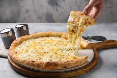 Photo of Woman taking piece of delicious cheese pizza at light grey table, closeup