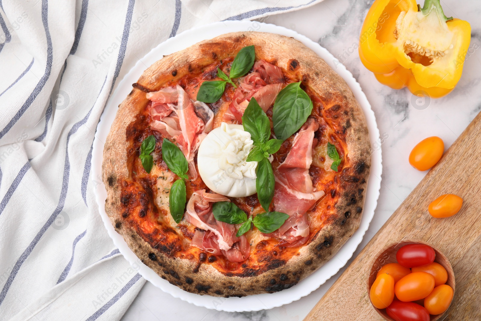 Photo of Delicious pizza with burrata cheese, basil, ham and vegetables on white marble table, flat lay