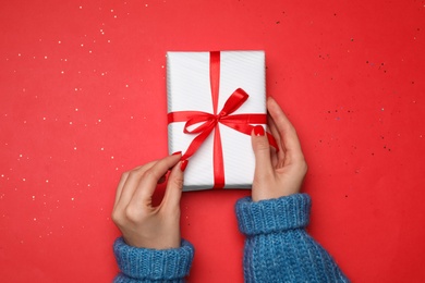 Young woman holding Christmas gift on red background, top view