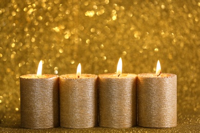 Stylish burning candles on gold shining background, space for text