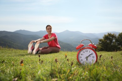 Young woman doing morning exercise in mountains, focus on alarm clock