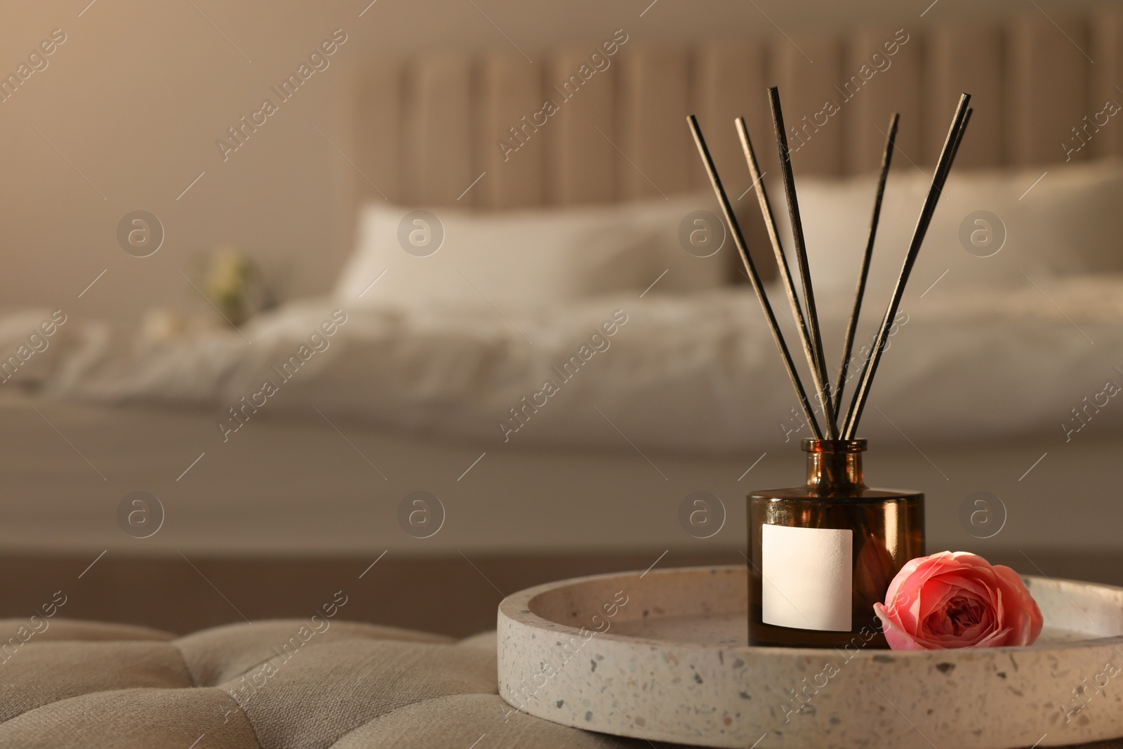 Photo of Aromatic reed air freshener and flower on bench in bedroom, space for text