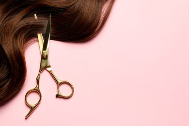 Professional hairdresser scissors with brown hair strand on pink background, top view. Space for text