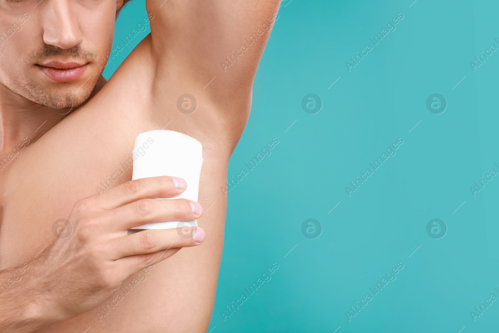 Photo of Young man applying deodorant to armpit on light blue background, closeup. Space for text