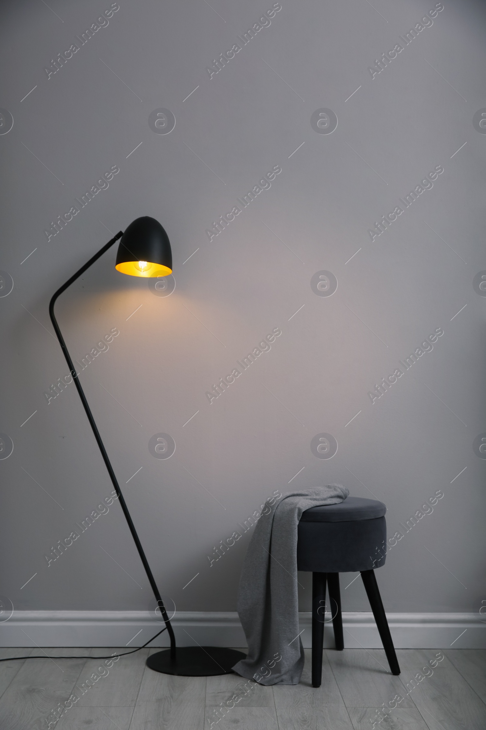 Photo of Modern floor lamp and ottoman near light grey wall indoors. Interior element