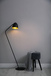 Photo of Modern floor lamp and ottoman near light grey wall indoors. Interior element