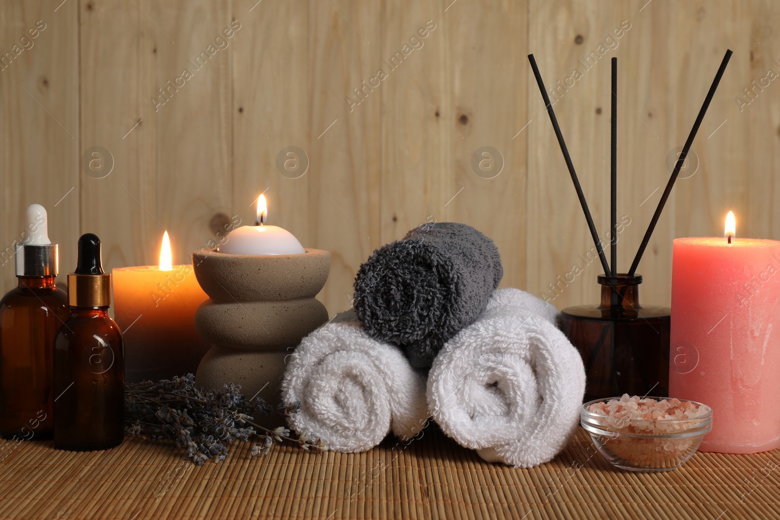 Photo of Aromatherapy. Scented candles, bottles, lavender, towels and sea salt on bamboo mat