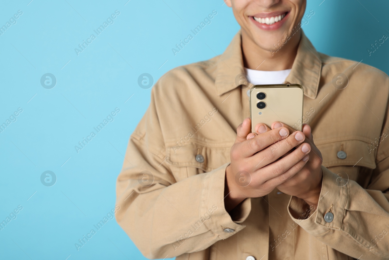 Photo of Young man sending message via smartphone on light blue background, closeup. Space for text