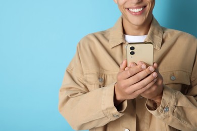 Photo of Young man sending message via smartphone on light blue background, closeup. Space for text