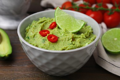 Bowl of delicious guacamole and ingredients on wooden table, closeup