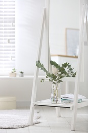 Photo of Vase with fresh eucalyptus branches on mirror shelf in room. Interior design
