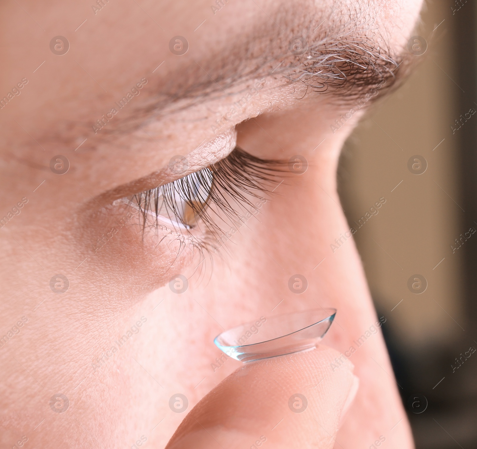 Photo of Young man putting contact lens in his eye, closeup