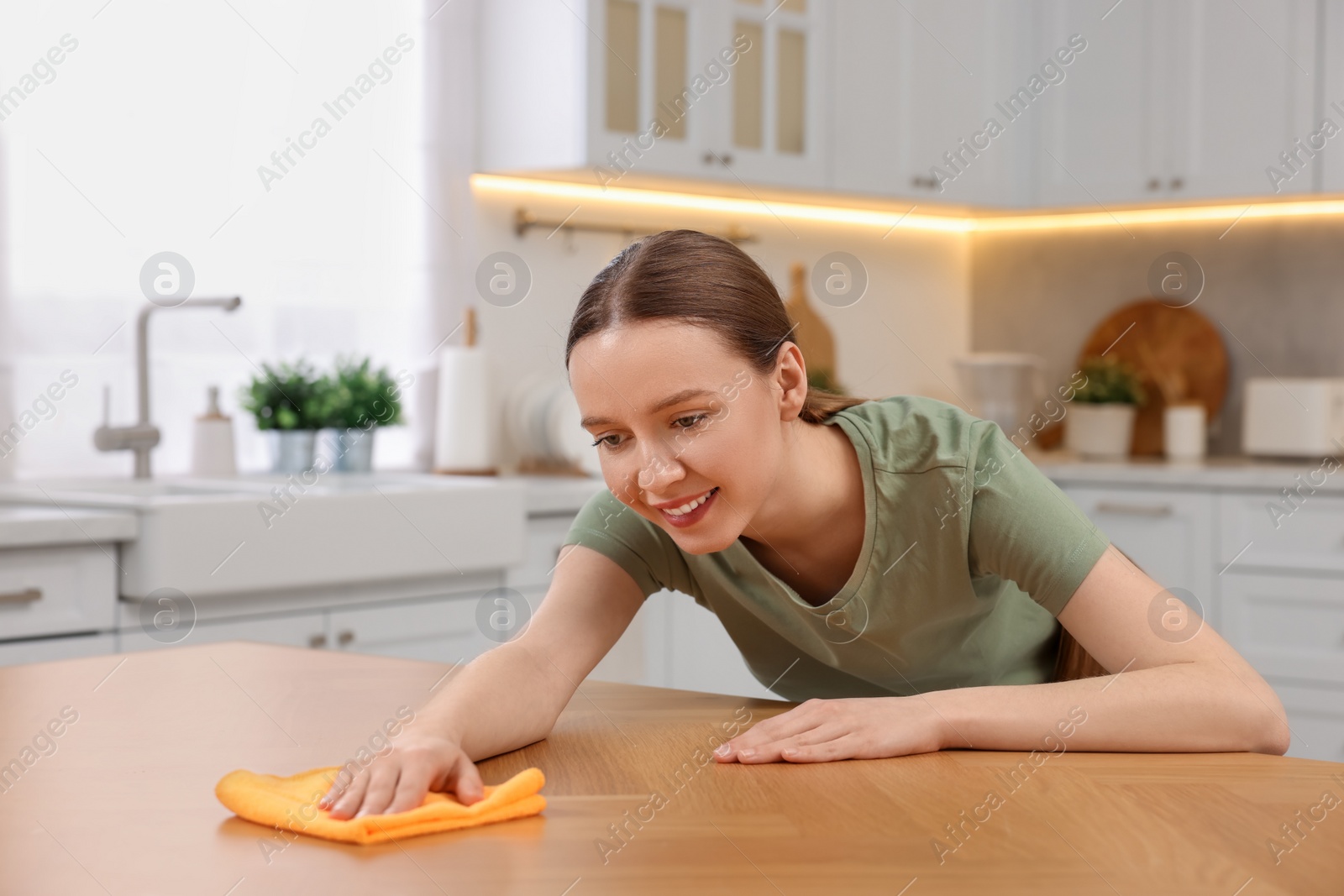 Photo of Woman with microfiber cloth cleaning wooden table in kitchen