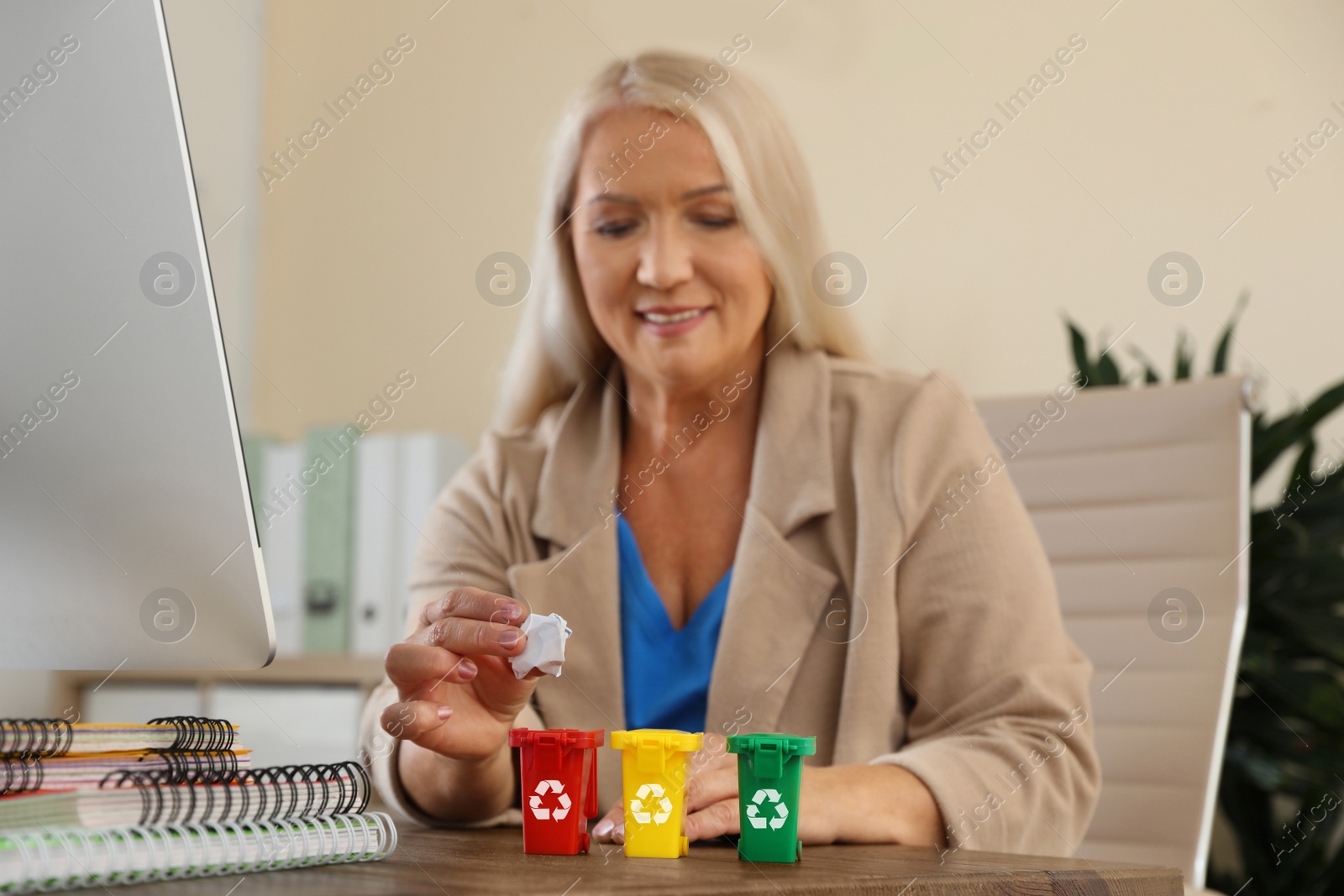 Photo of Woman throwing paper into mini recycling bin at office