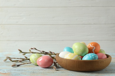 Plate with painted Easter eggs on table against wooden background, space for text